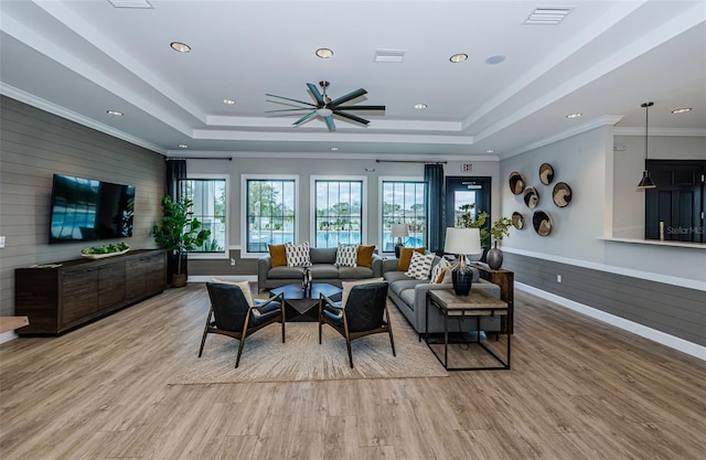 living room featuring crown molding, a raised ceiling, visible vents, and light wood-style floors