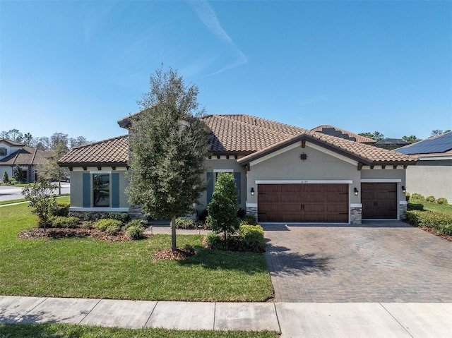 mediterranean / spanish home featuring decorative driveway, a front yard, stone siding, and an attached garage