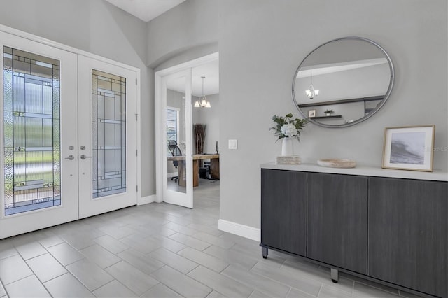 foyer featuring baseboards, a chandelier, and french doors