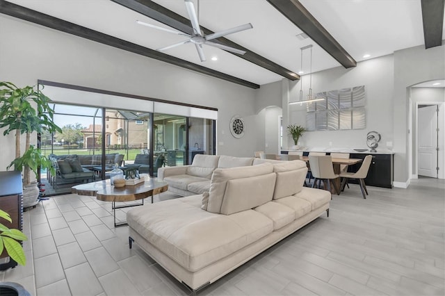 living room with a ceiling fan, baseboards, arched walkways, and beamed ceiling