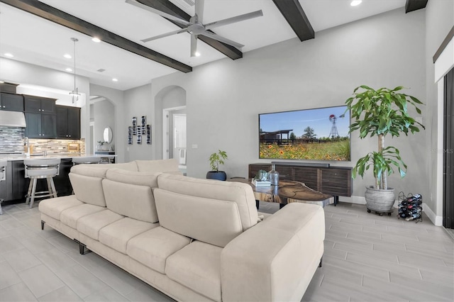 living room featuring a ceiling fan, arched walkways, beamed ceiling, and recessed lighting