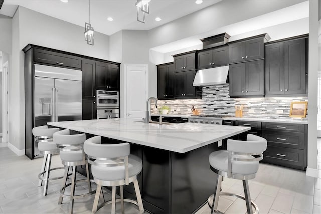 kitchen with stainless steel appliances, backsplash, a sink, dark cabinets, and under cabinet range hood