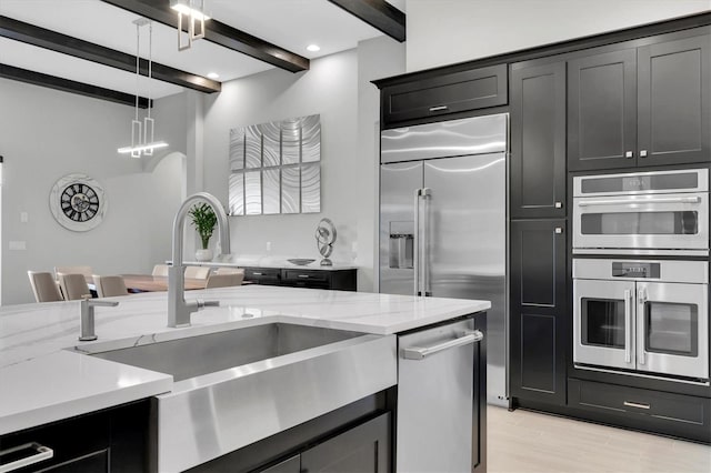 kitchen featuring appliances with stainless steel finishes, beamed ceiling, decorative light fixtures, light stone countertops, and a sink