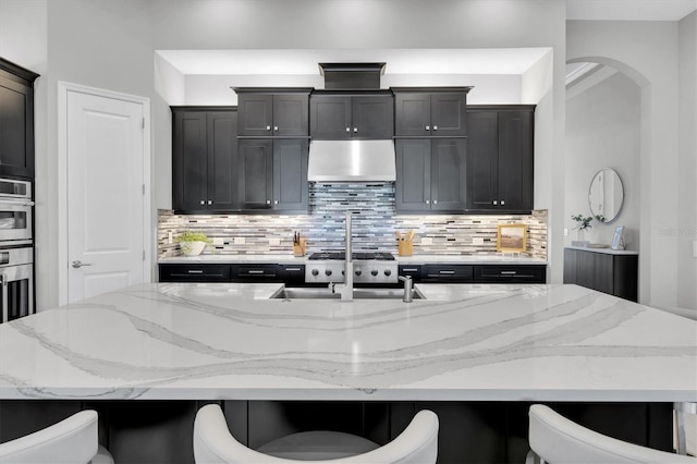 kitchen with backsplash, under cabinet range hood, a kitchen bar, and light stone countertops