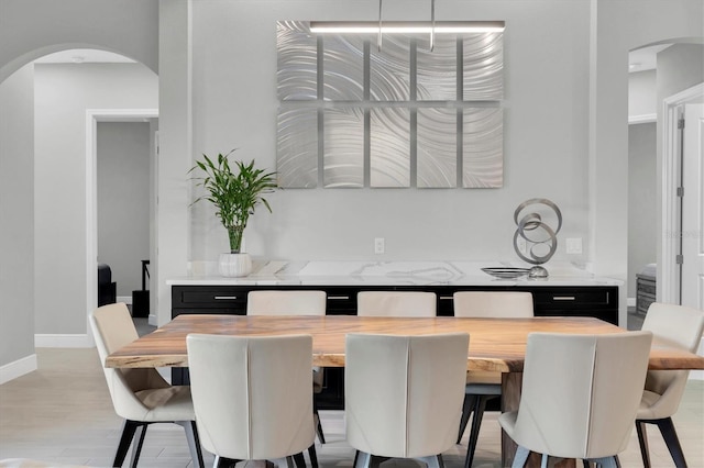 dining area with light wood-type flooring, arched walkways, and baseboards