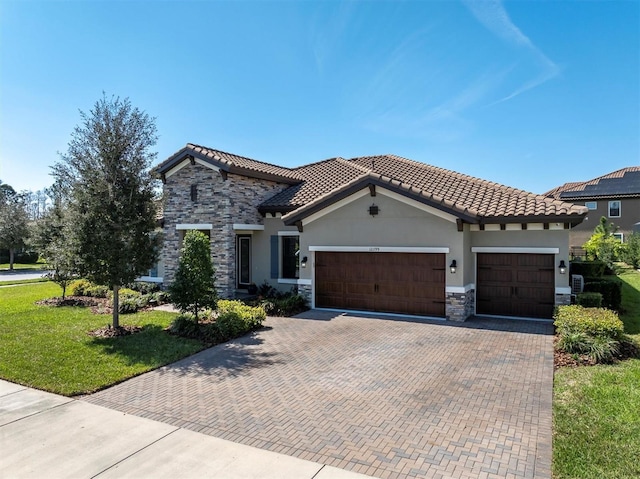 mediterranean / spanish-style home with decorative driveway, stucco siding, a front yard, a garage, and stone siding