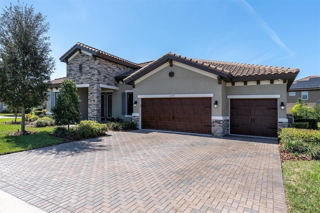 mediterranean / spanish home featuring a garage, stone siding, decorative driveway, and stucco siding