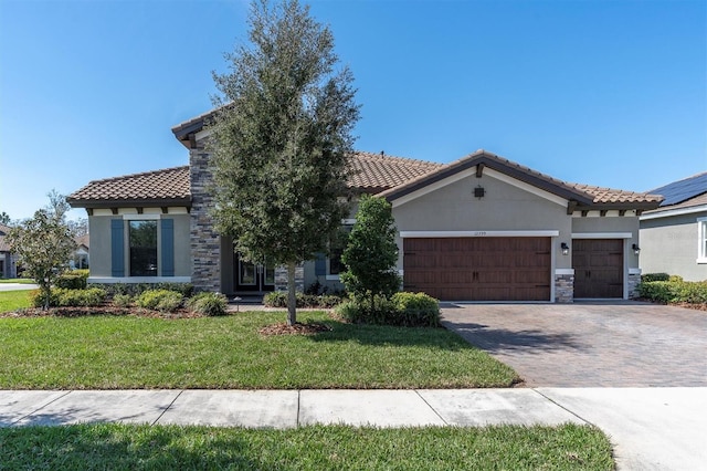 mediterranean / spanish home featuring decorative driveway, stucco siding, a garage, stone siding, and a front lawn