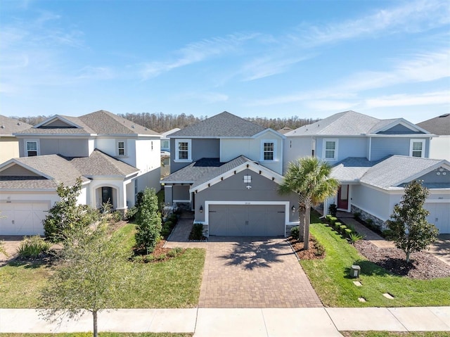 traditional home featuring a garage, a residential view, decorative driveway, and stucco siding