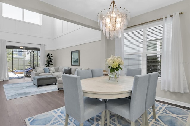 dining space featuring baseboards, a towering ceiling, an inviting chandelier, and wood finished floors