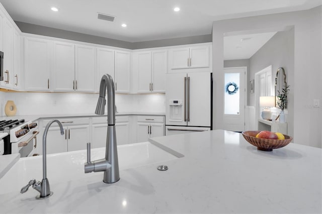 kitchen featuring white appliances, visible vents, white cabinets, a sink, and recessed lighting