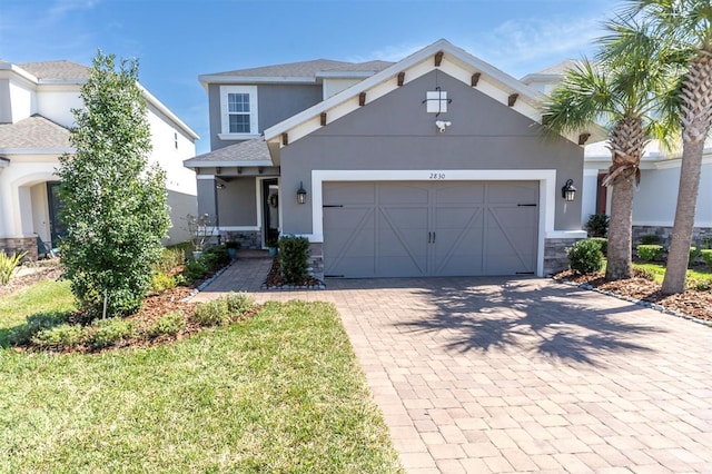 view of front of house with a garage, stone siding, decorative driveway, and stucco siding