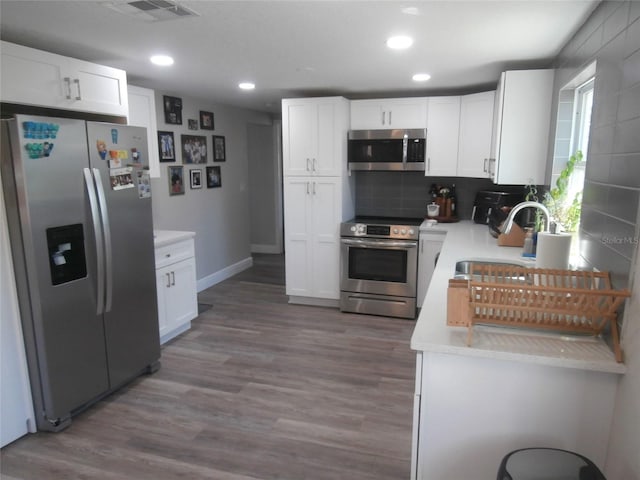 kitchen featuring light countertops, appliances with stainless steel finishes, wood finished floors, white cabinets, and a sink