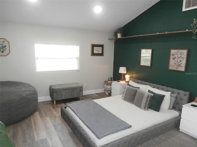 bedroom with vaulted ceiling, wood finished floors, visible vents, and baseboards