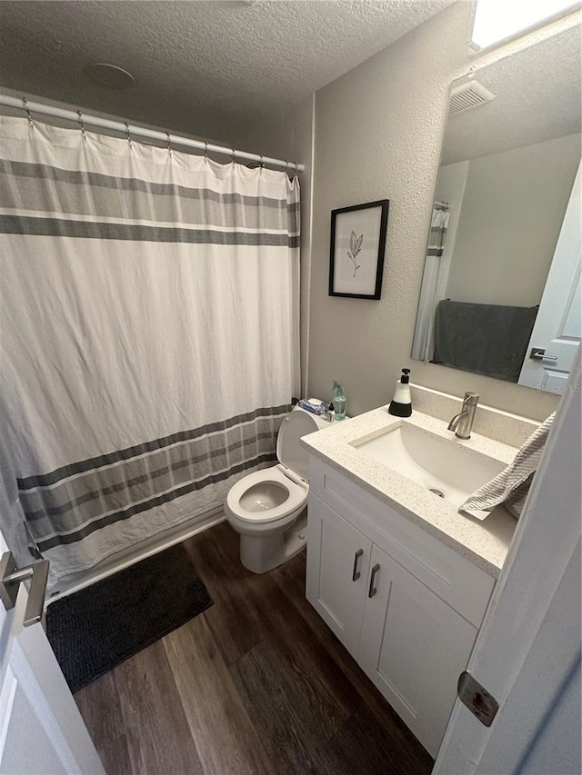 bathroom with toilet, a shower with shower curtain, vanity, wood finished floors, and a textured ceiling