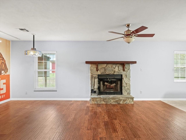 unfurnished living room with visible vents, ceiling fan, a stone fireplace, wood finished floors, and baseboards