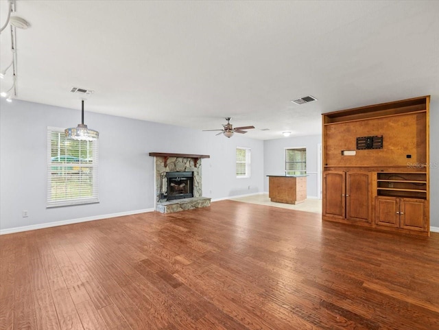 unfurnished living room featuring a ceiling fan, a fireplace, visible vents, and wood finished floors