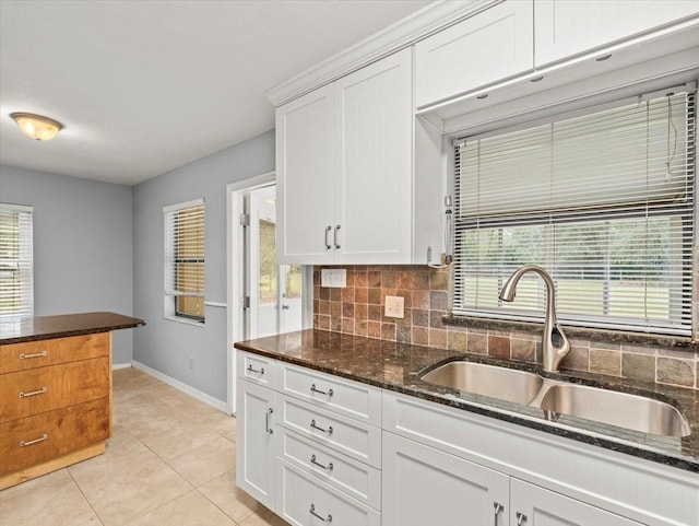 kitchen featuring light tile patterned floors, decorative backsplash, white cabinets, a sink, and dark stone countertops