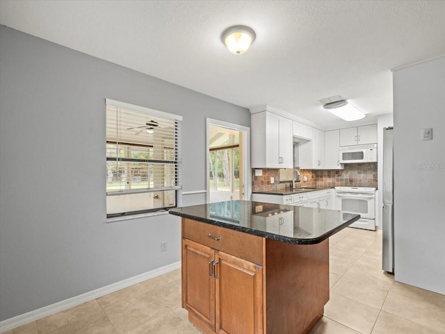 kitchen featuring white appliances, tasteful backsplash, a kitchen island, white cabinetry, and a sink