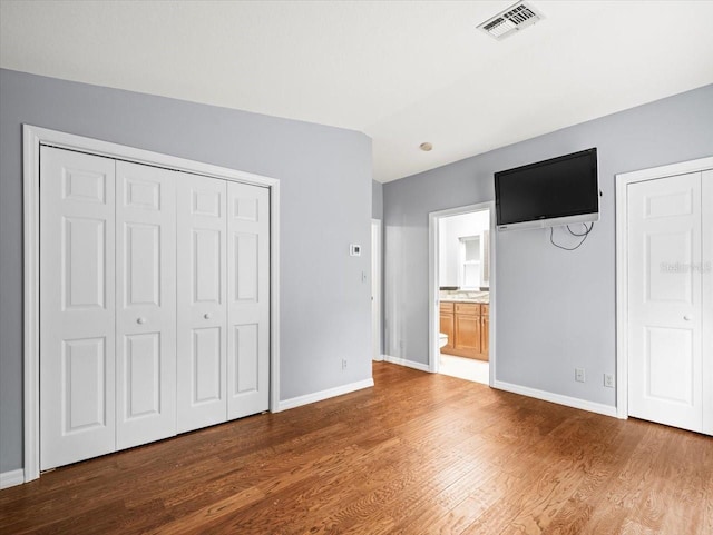 unfurnished bedroom with ensuite bath, baseboards, visible vents, and wood finished floors