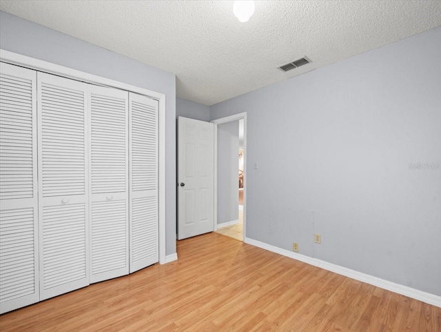 unfurnished bedroom with light wood finished floors, baseboards, visible vents, a textured ceiling, and a closet