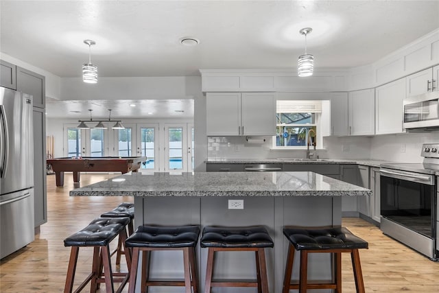 kitchen featuring backsplash, light wood-style flooring, appliances with stainless steel finishes, a sink, and a kitchen bar