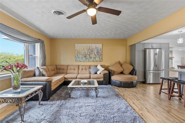 living room with a textured ceiling, a ceiling fan, visible vents, and light wood-style floors