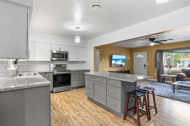 kitchen featuring appliances with stainless steel finishes, a center island, light wood-style flooring, and gray cabinetry