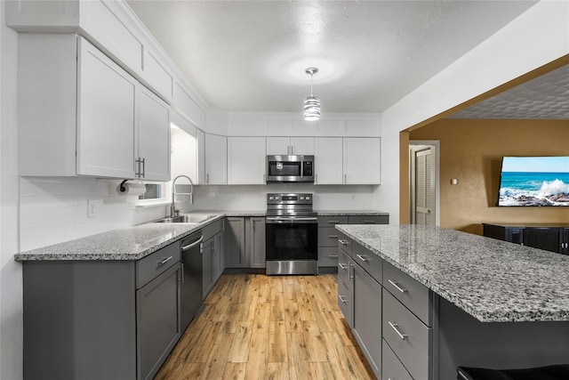 kitchen featuring light wood finished floors, light stone counters, stainless steel appliances, gray cabinetry, and a sink