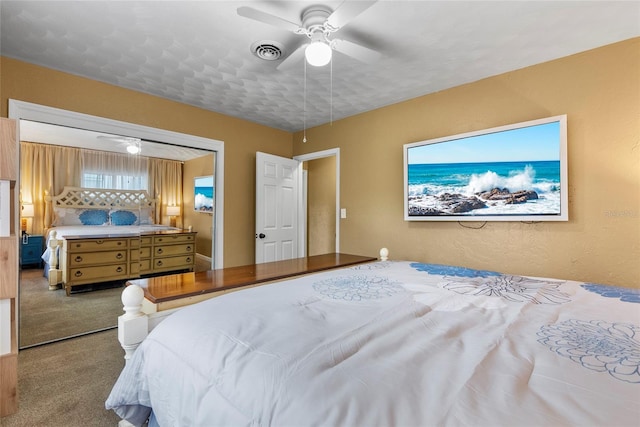 bedroom with ceiling fan, a textured wall, carpet flooring, and visible vents