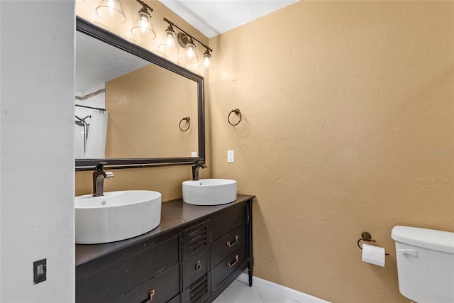 full bath with a textured wall, a sink, toilet, and double vanity