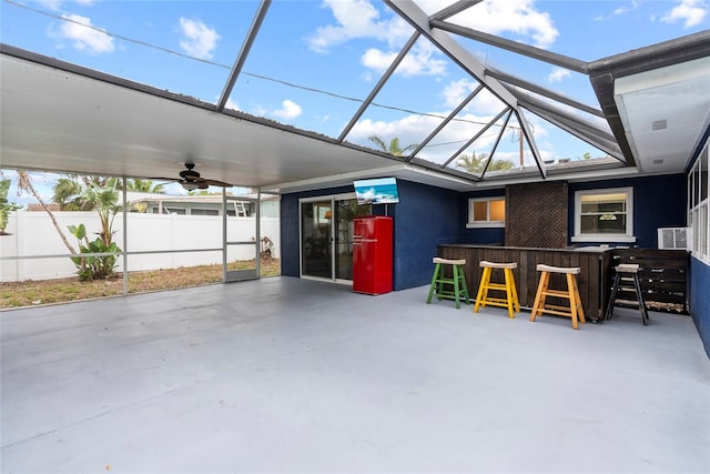 view of patio with outdoor dry bar, a lanai, a ceiling fan, and fence