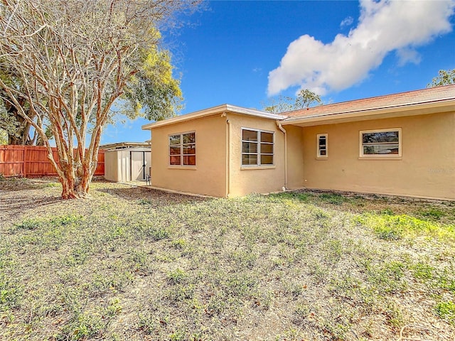 view of side of property featuring fence, a storage unit, an outdoor structure, and stucco siding