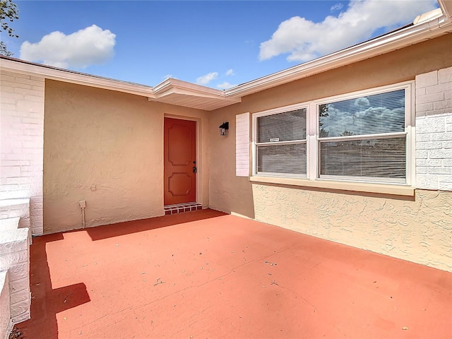 view of exterior entry with a patio area and stucco siding