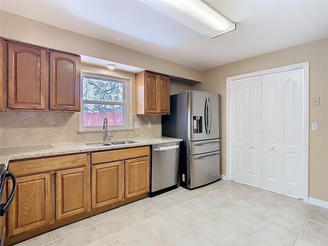 kitchen with a sink, baseboards, appliances with stainless steel finishes, backsplash, and brown cabinetry