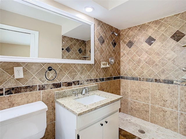 full bath featuring vanity, a tile shower, toilet, and tile walls