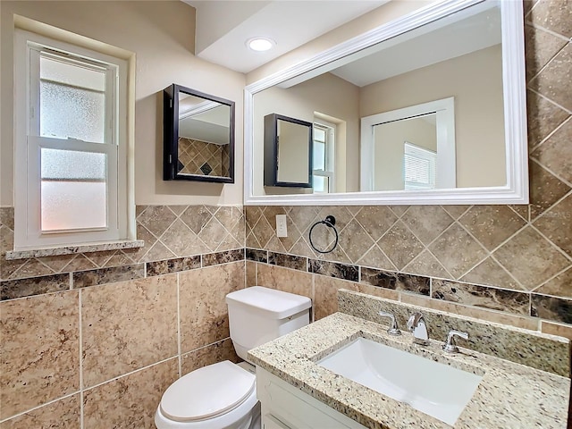 bathroom featuring toilet, plenty of natural light, tile walls, and vanity