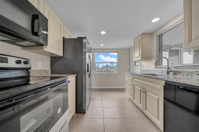 kitchen featuring cream cabinetry, black appliances, a sink, light tile patterned flooring, and baseboards