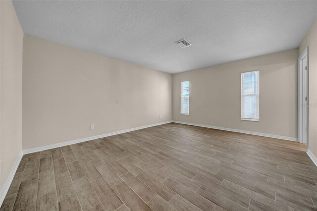 unfurnished room with visible vents, a textured ceiling, baseboards, and wood finished floors