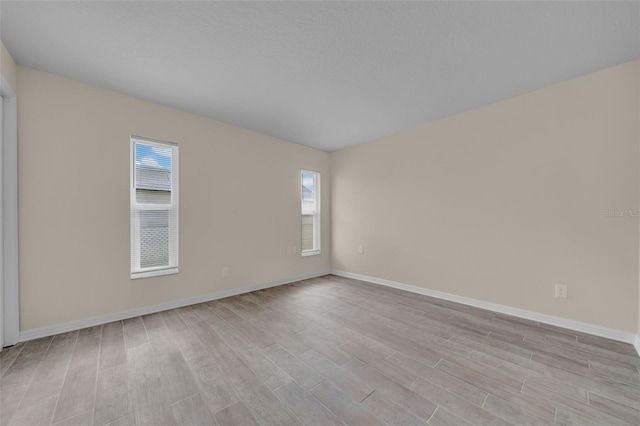 spare room with baseboards and light wood finished floors