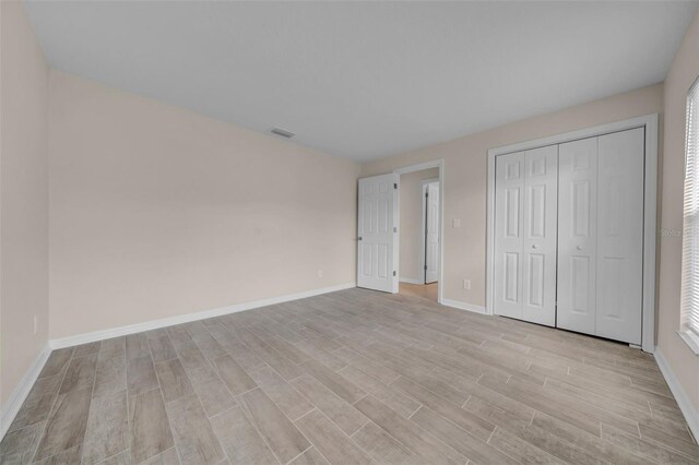 unfurnished bedroom with light wood-type flooring, baseboards, visible vents, and a closet