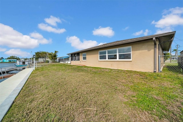 view of property exterior with stucco siding, a dock, a yard, and fence