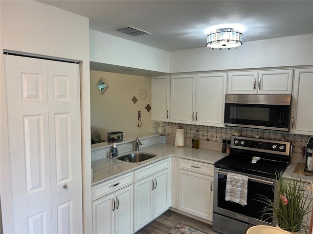 kitchen with stainless steel appliances, visible vents, dark wood-type flooring, white cabinets, and a sink