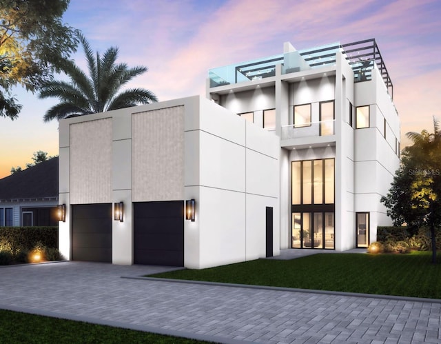 contemporary home with a front lawn, decorative driveway, an attached garage, and stucco siding