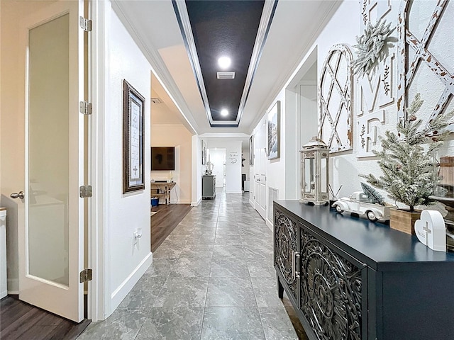 hallway with a tray ceiling, visible vents, crown molding, and baseboards