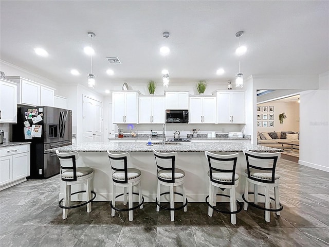 kitchen with a kitchen island with sink, visible vents, a kitchen breakfast bar, white cabinets, and stainless steel fridge