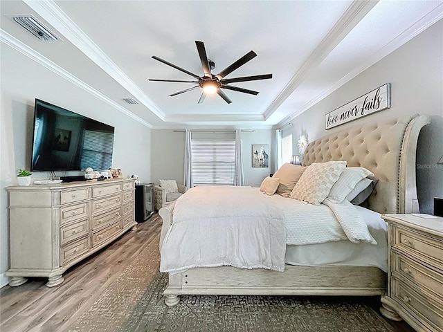 bedroom with ornamental molding, wood finished floors, a raised ceiling, and visible vents