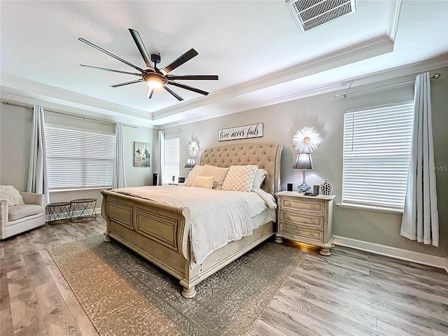 bedroom with light wood finished floors, a raised ceiling, and visible vents