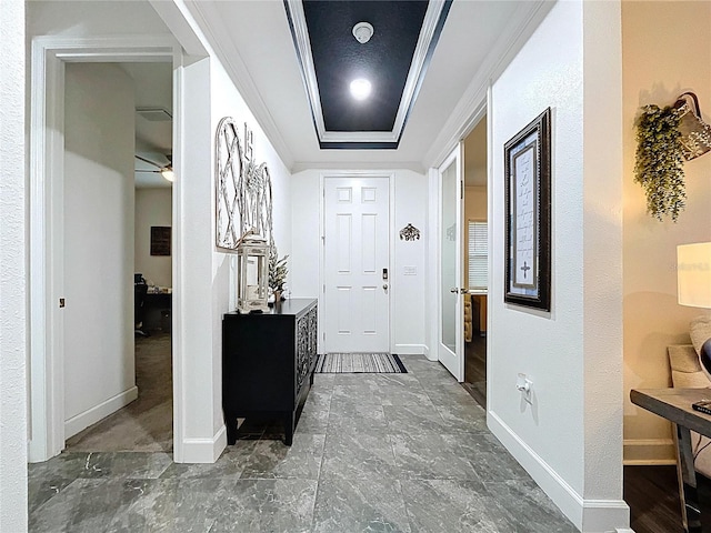 foyer entrance featuring a tray ceiling, crown molding, and baseboards