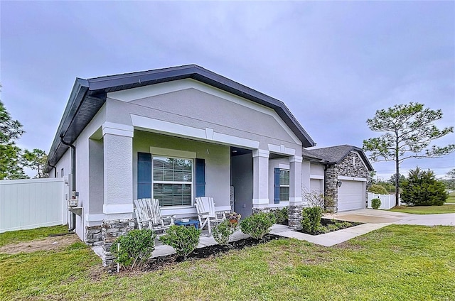 view of front of house with stucco siding, covered porch, an attached garage, fence, and stone siding